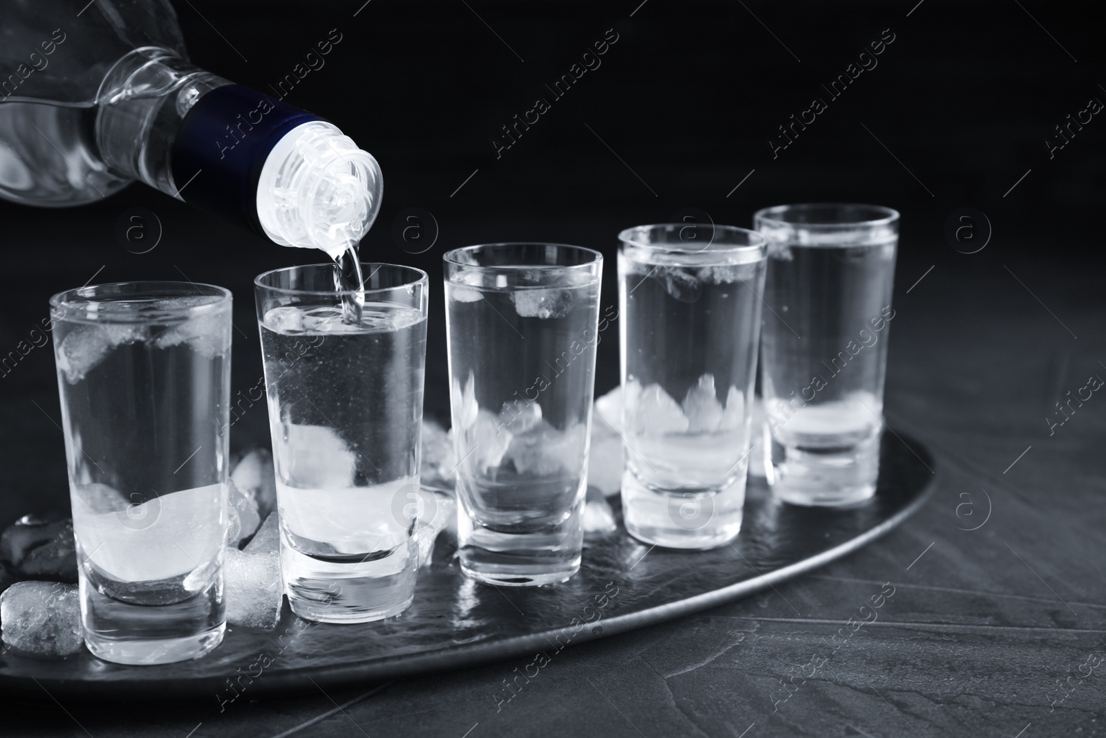 Photo of Pouring vodka from bottle into shot glass on grey table