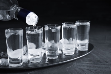 Pouring vodka from bottle into shot glass on grey table