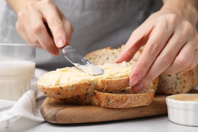 Photo of Woman spreading tasty butter onto bread at table, closeup