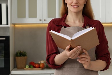 Photo of Woman with recipe book in kitchen, closeup. Space for text