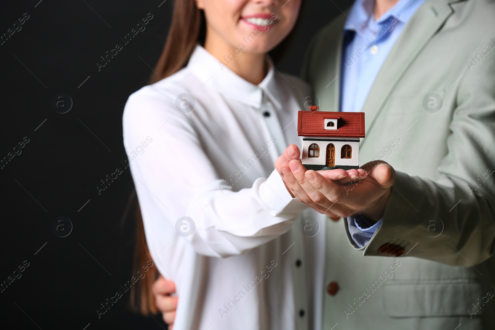 Photo of Young couple holding house model on black background, closeup. Home insurance