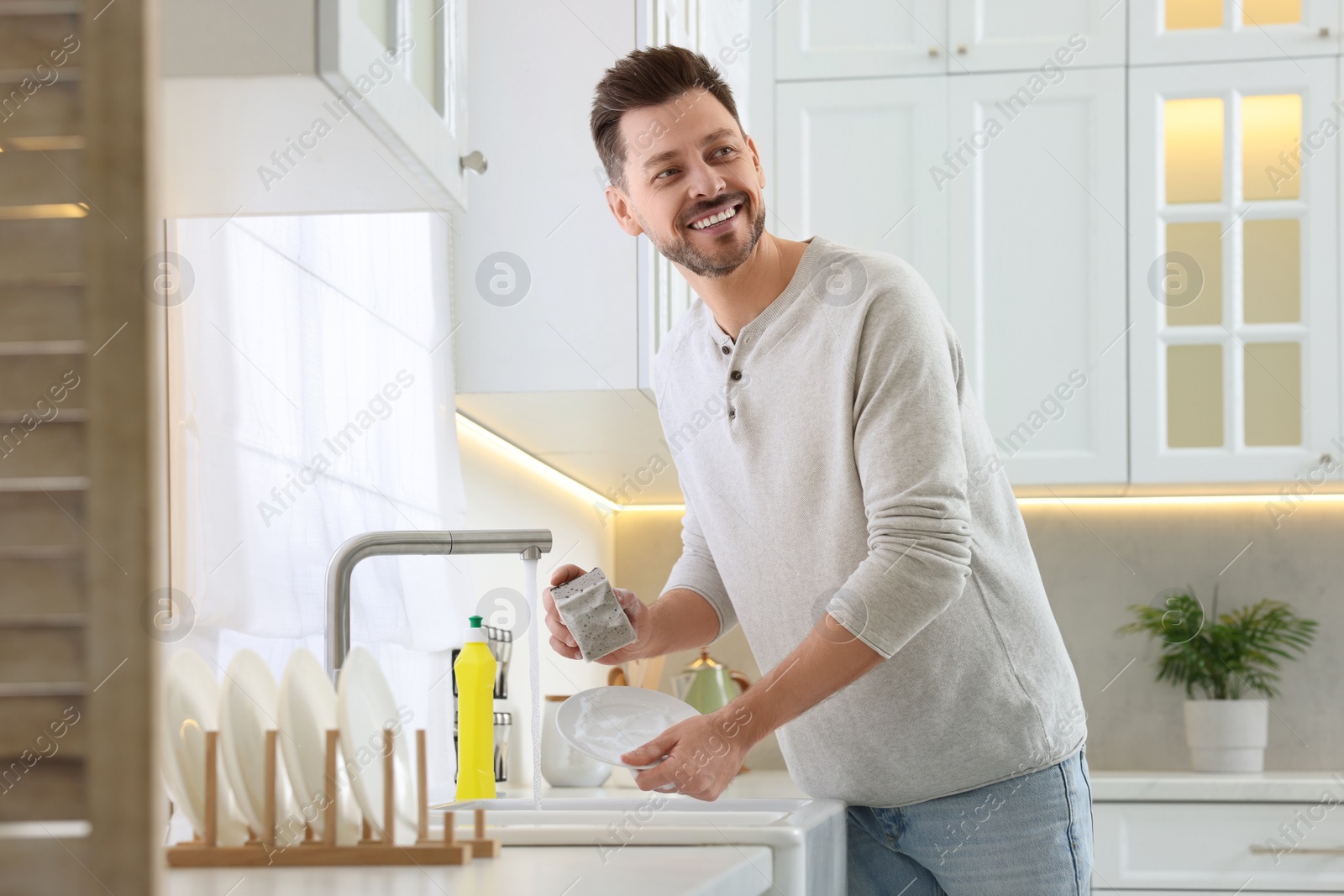 Photo of Man washing plate above sink in kitchen