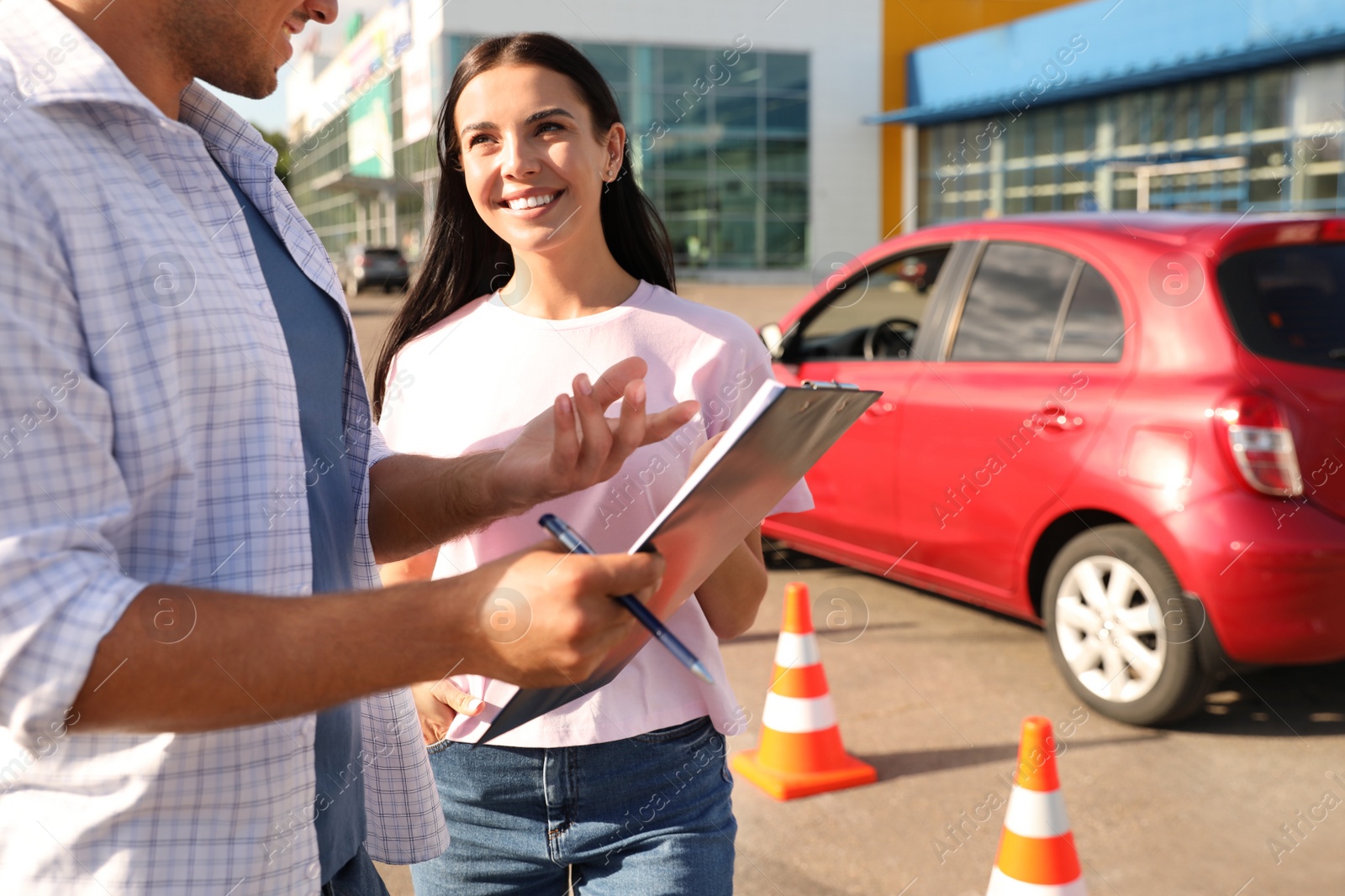 Photo of Instructor with clipboard and his student near car outdoors. Driving school exam