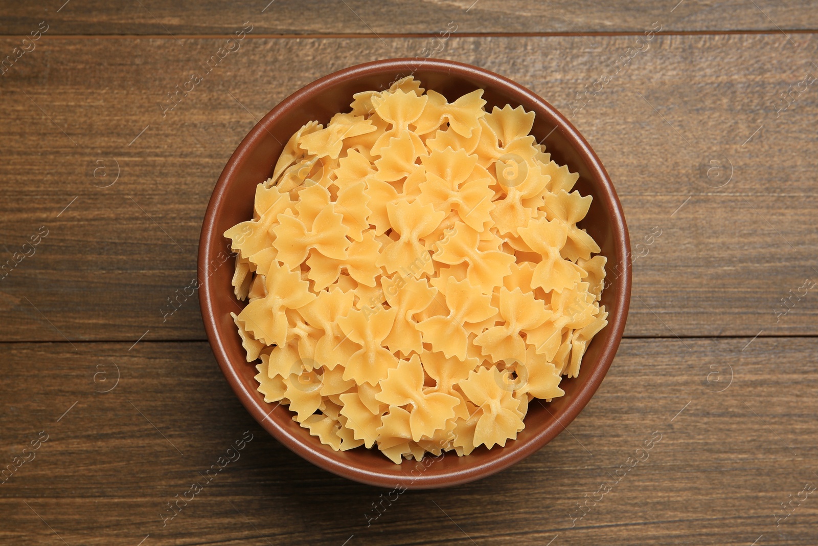 Photo of Raw farfalle pasta in bowl on wooden table, top view