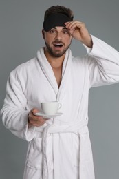 Photo of Young man in bathrobe with cup of coffee on grey background