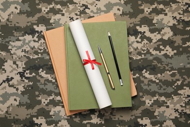 Photo of Notebooks, diploma, pen and pencil on camouflage fabric, top view. Military education