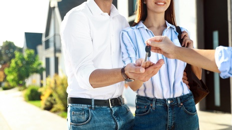 Photo of Real estate agent giving house keys to young couple outdoors, closeup