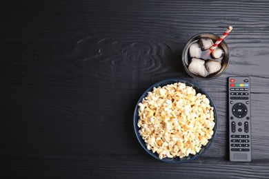 Bowl with popcorn, glass of iced cola and TV remote on wooden background, top view with space for text. Watching cinema