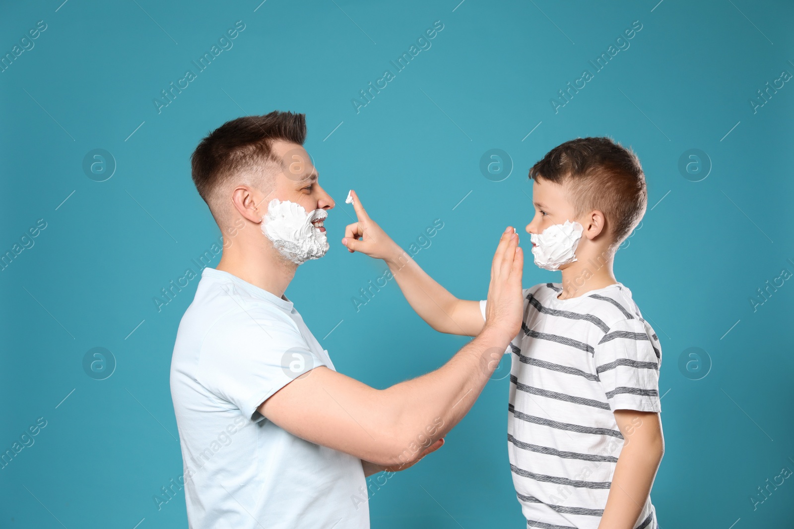 Photo of Happy dad and son with shaving foam on faces against blue background