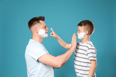 Happy dad and son with shaving foam on faces against blue background