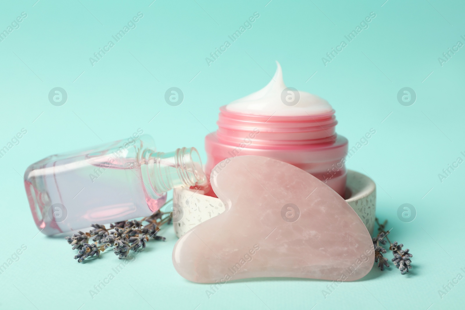 Photo of Rose quartz gua sha tool, cosmetic products and dried lavender flowers on light blue background