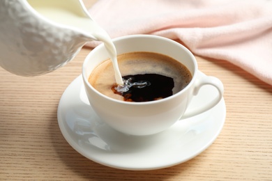 Pouring milk into cup of hot coffee on wooden table