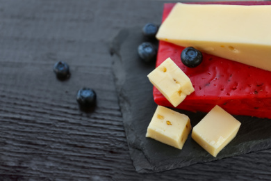 Photo of Different delicious cheeses and blueberries on black wooden table, closeup