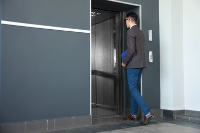 Photo of Young businessman entering modern elevator, back view