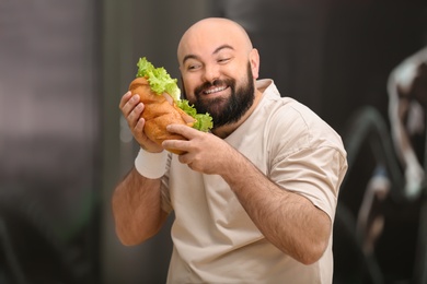 Overweight man eating sandwich in gym