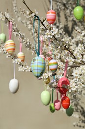 Photo of Beautifully painted Easter eggs hanging on blooming cherry tree outdoors