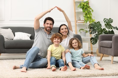 Family housing concept. Happy woman and her husband forming roof with their hands while sitting with kids on floor at home