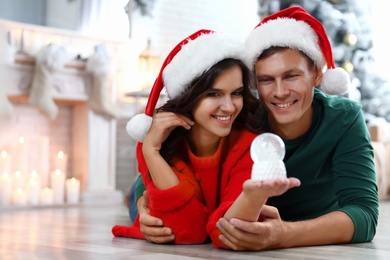 Happy couple with snow globe on floor at home