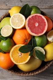 Different fresh citrus fruits and leaves in wicker basket on wooden table, top view