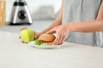 Woman with tasty sandwich and fresh apple at table. Choice between diet and unhealthy food