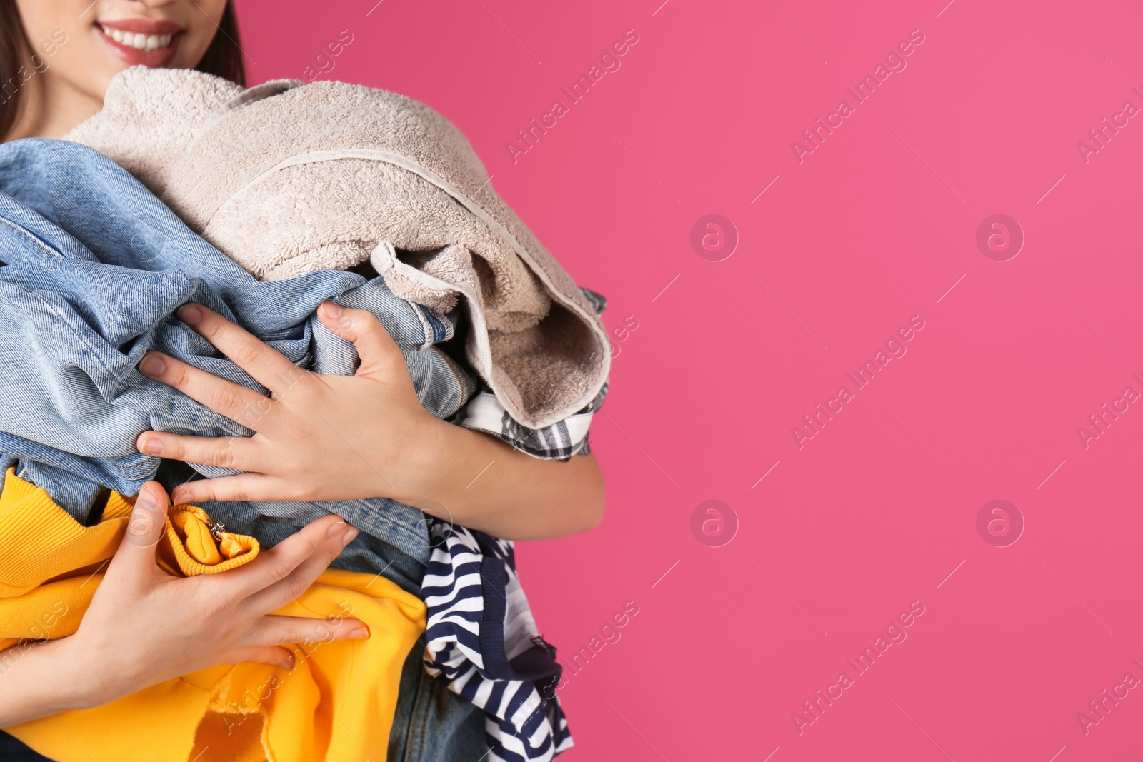 Photo of Young woman holding pile of dirty laundry on color background, closeup. Space for text