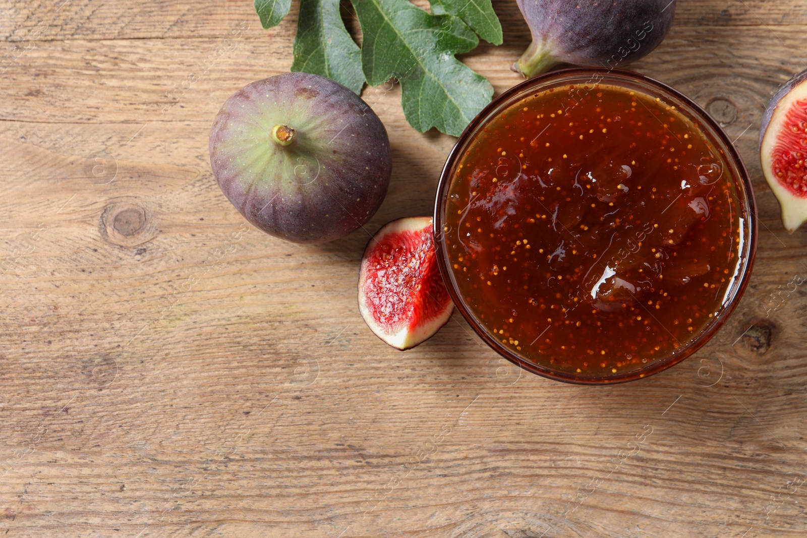 Photo of Bowl with tasty sweet jam and fresh figs on wooden table, flat lay. Space for text