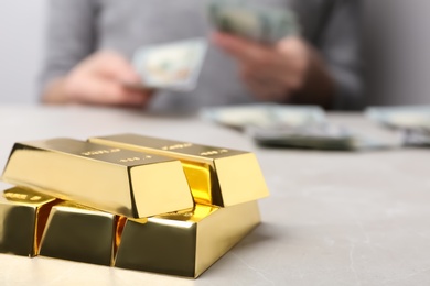 Photo of Stacked gold bars and woman counting money at table, closeup. Space for text