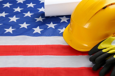 Photo of Yellow protective hard hat, gloves and construction drawing on American flag. Space for text