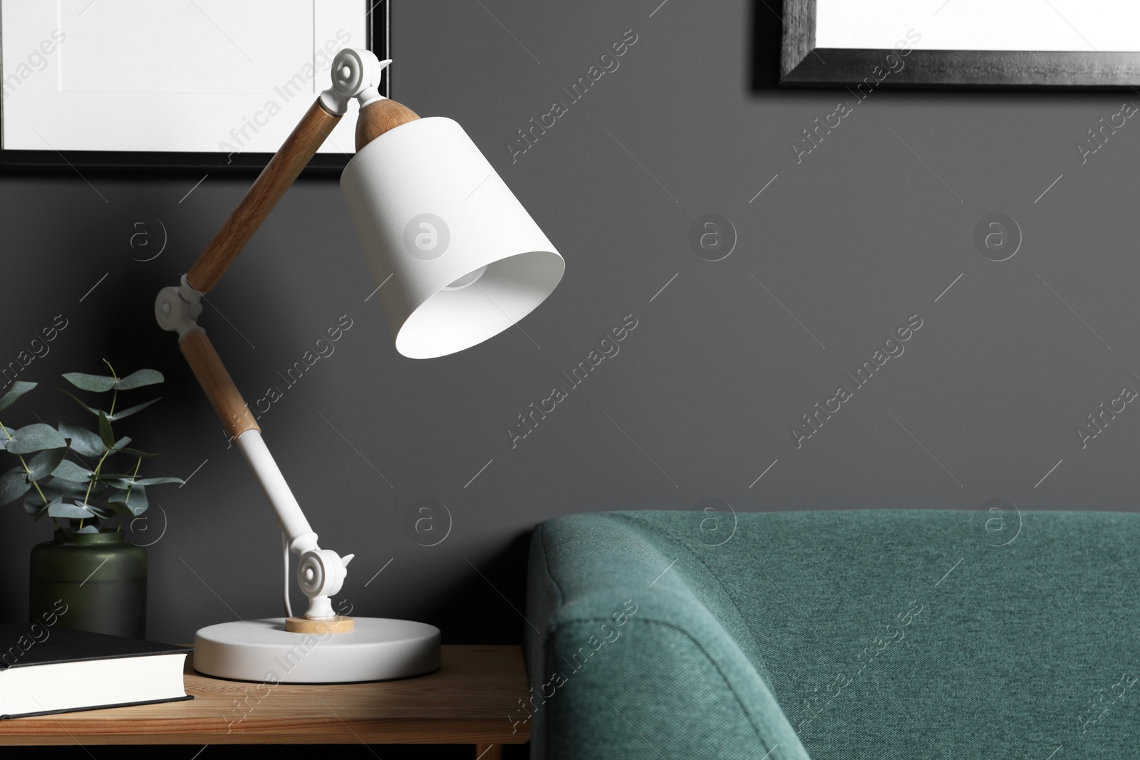 Photo of Stylish modern desk lamp, book and plant on wooden cabinet in living room