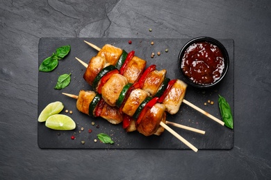 Photo of Delicious chicken shish kebabs with vegetables and sauce on black table, flat lay