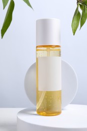 Bottle of cosmetic product and leaves on white wooden table