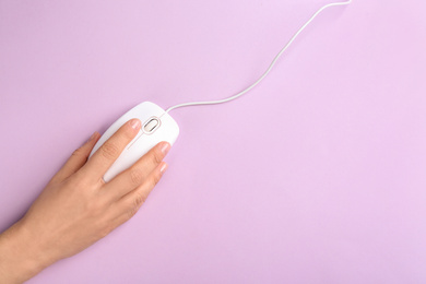 Woman using modern wired optical mouse on lilac background, top view. Space for text