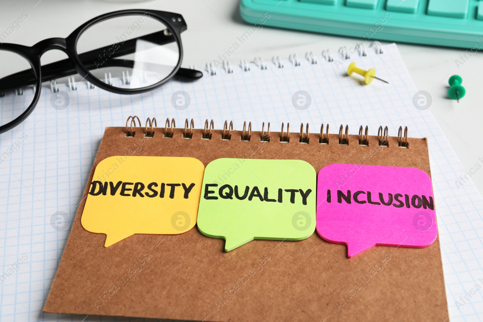 Photo of Sticky notes with words Diversity, Equality, Inclusion, notebooks and glasses on white table, closeup