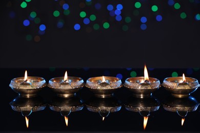 Photo of Many lit diyas on dark background with blurred lights, space for text. Diwali lamps