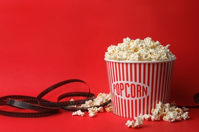 Bucket of fresh popcorn and film footage on red background, space for text. Cinema snack