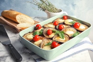 Photo of Baked eggplant with tomatoes, cheese and basil in dishware on marble table