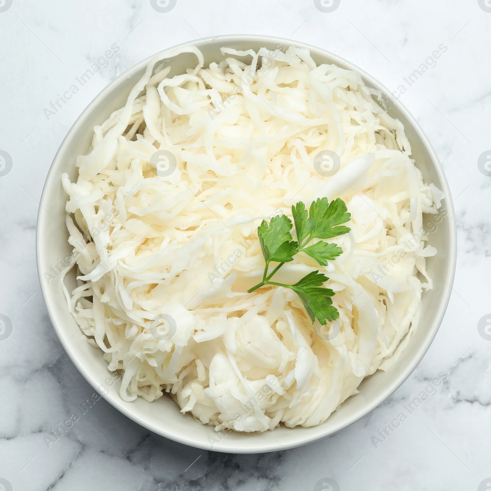 Photo of Tasty fermented cabbage with parsley on white marble table, top view