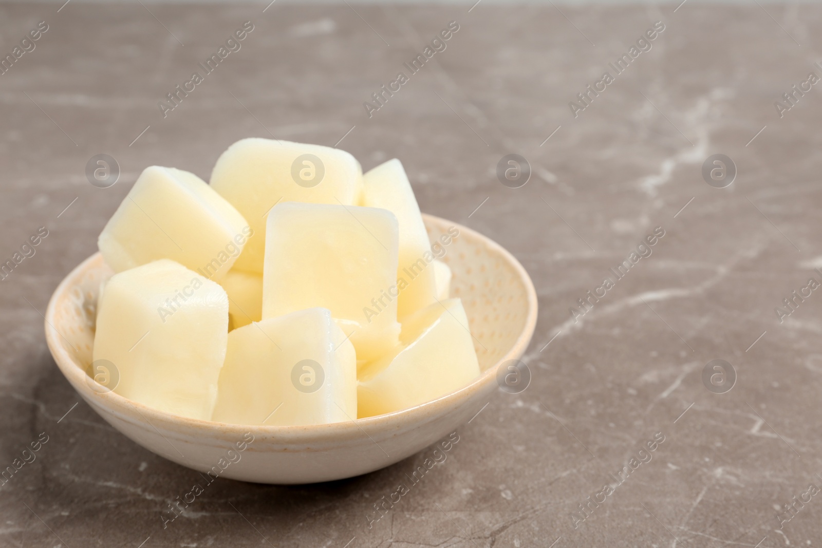 Photo of Bowl with milk ice cubes on grey table. Space for text
