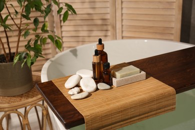 Photo of Wooden tray with spa products and stones on bath tub in bathroom