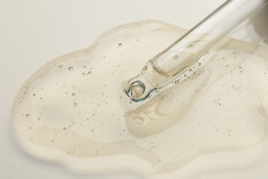 Photo of Dripping cosmetic oil from pipette onto beige background, closeup