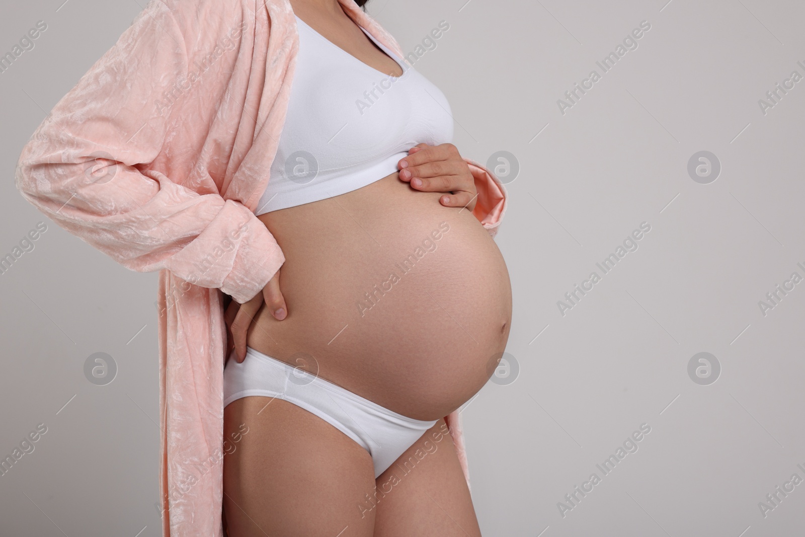 Photo of Pregnant woman in stylish comfortable underwear and robe on grey background, closeup. Space for text