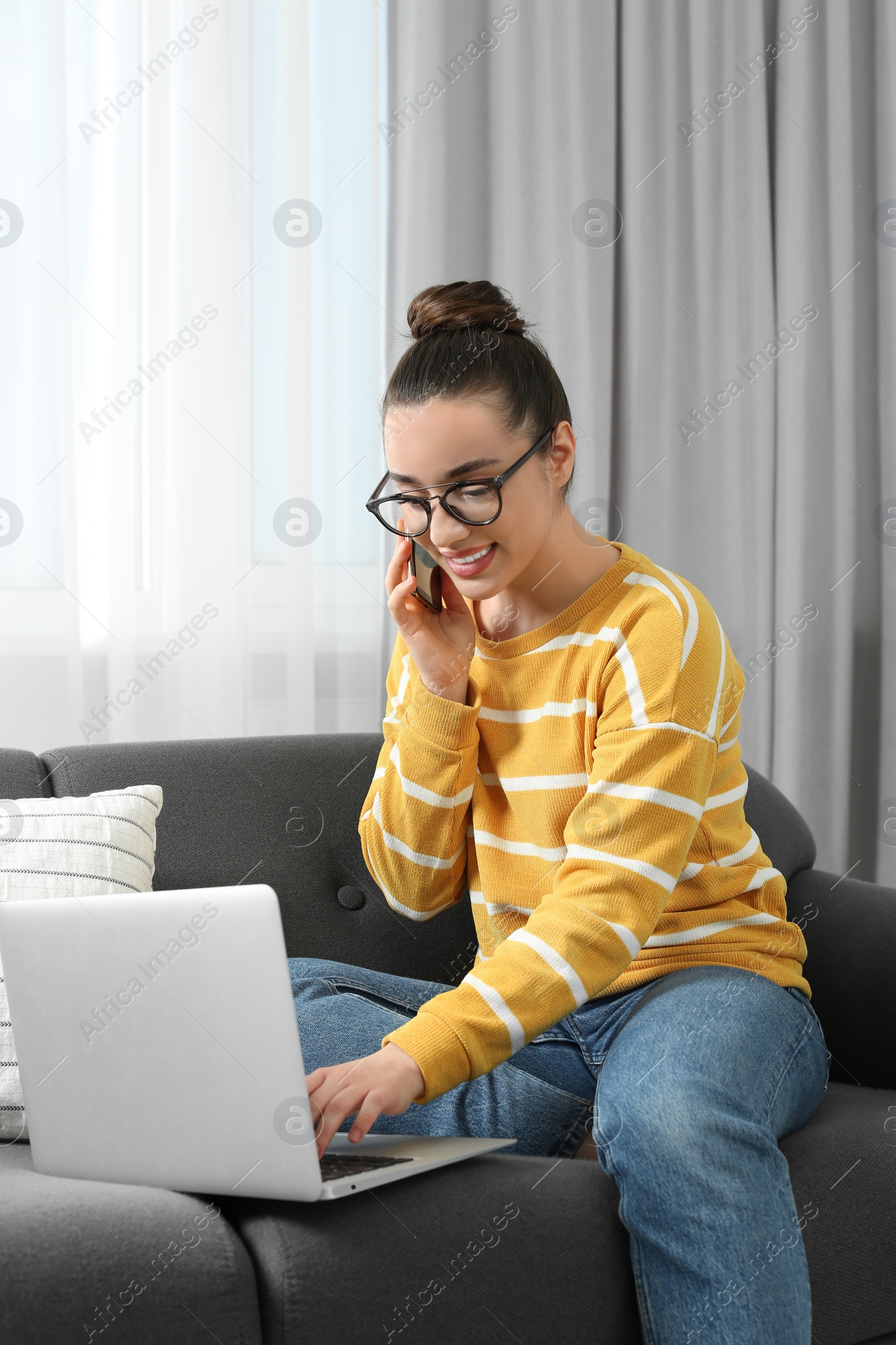 Photo of Home workplace. Happy woman talking on smartphone while working on laptop in room