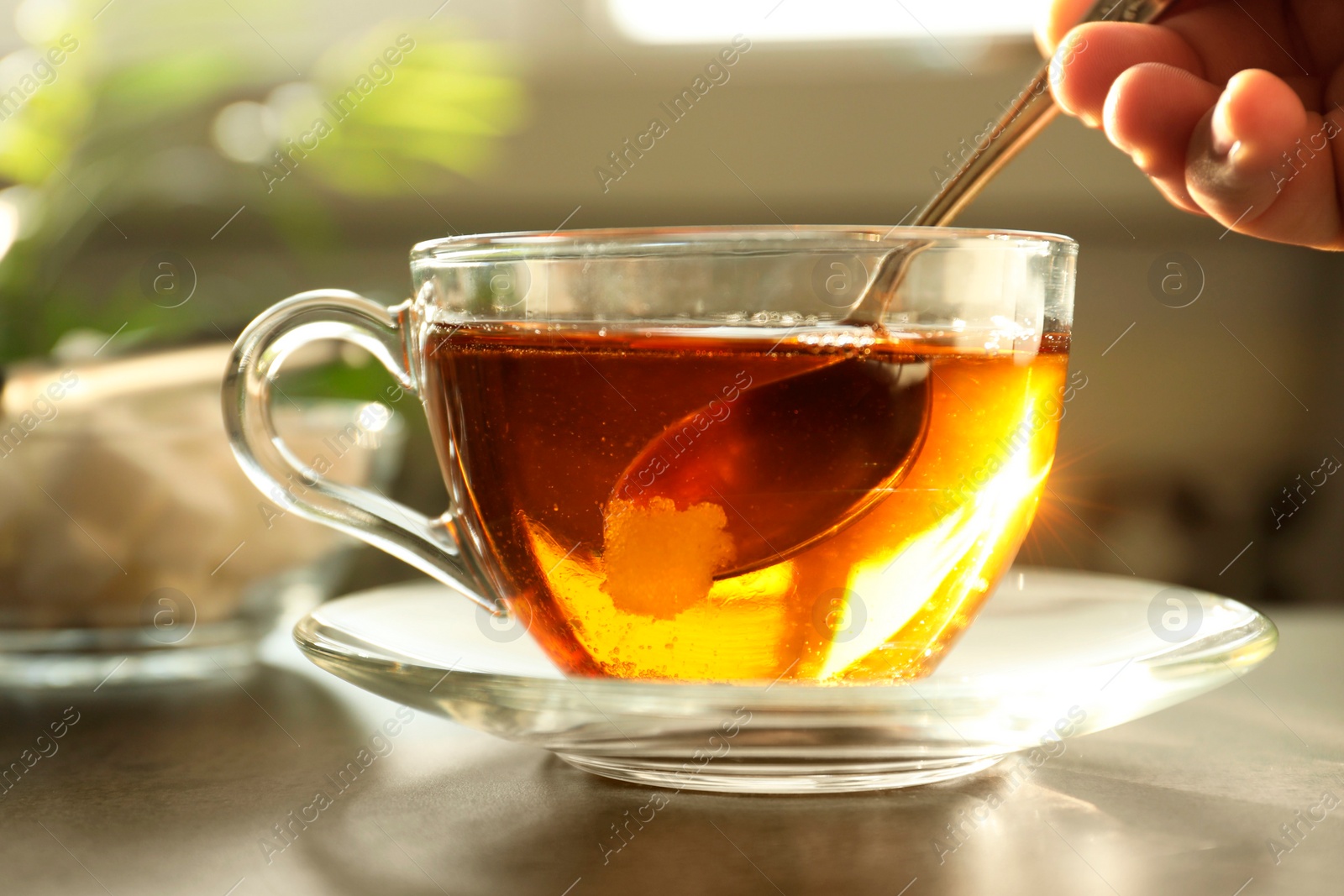 Photo of Woman adding sugar into cup of tea at table, closeup