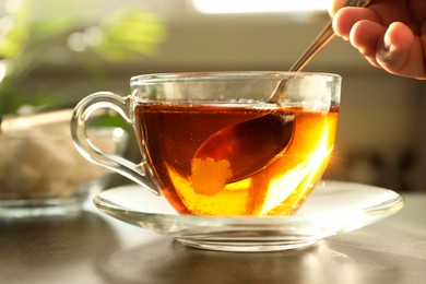 Woman adding sugar into cup of tea at table, closeup