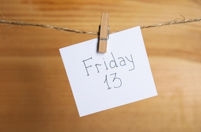 Photo of Paper note with phrase Friday 13 hanging on twine against wooden background. Bad luck superstition