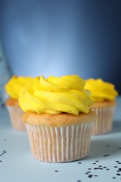 Photo of Delicious cupcakes with bright cream and confetti on blue background, closeup