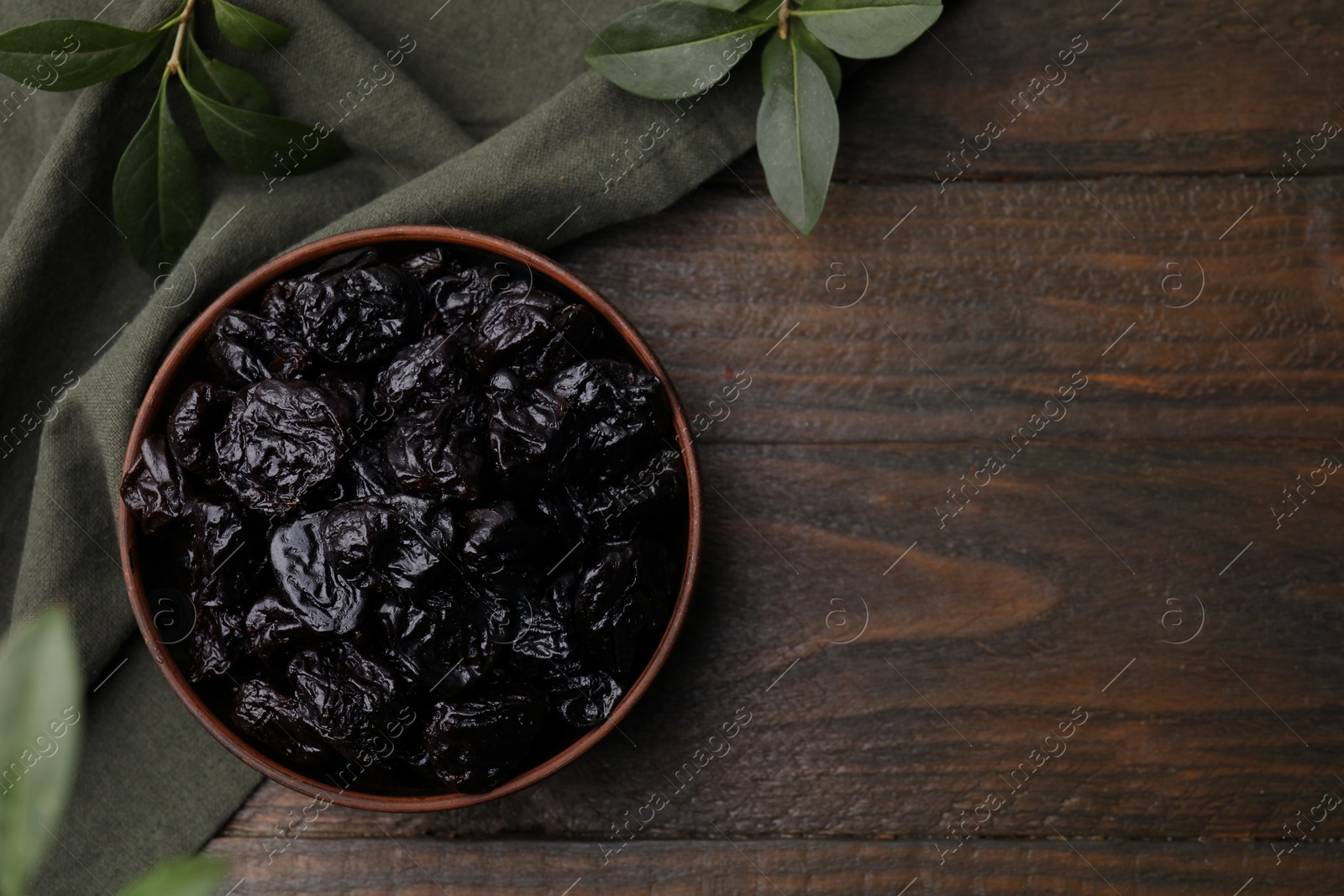 Photo of Sweet dried prunes in bowl on wooden table, top view. Space for text