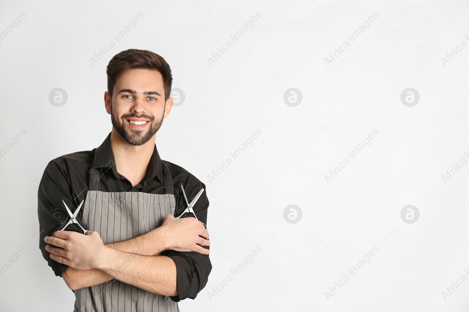 Photo of Young hairstylist holding professional scissors on light background