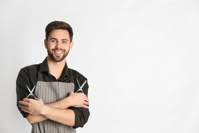 Photo of Young hairstylist holding professional scissors on light background