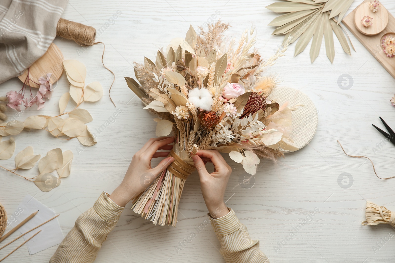 Photo of Florist making beautiful bouquet of dried flowers at white table, top view